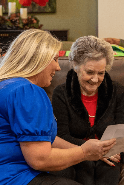 A Carlton Senior Living staff member sitting with a senior resident, looking at a photograph together as part of a memory care activity.